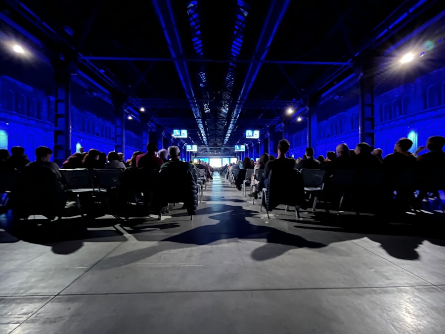 Crowded auditorium under blue stage lighting with people attending a tech summit event