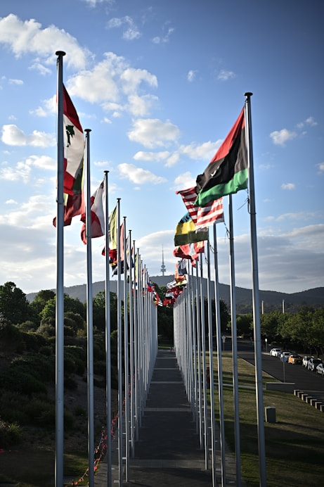 Row of tall flagpoles with colorful international flags fluttering outside a large modern event venue on a sunny day